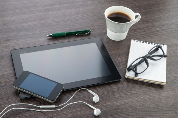 Smartphone und Tablet liegen neben Brille und Kaffee auf hölzernem Tisch